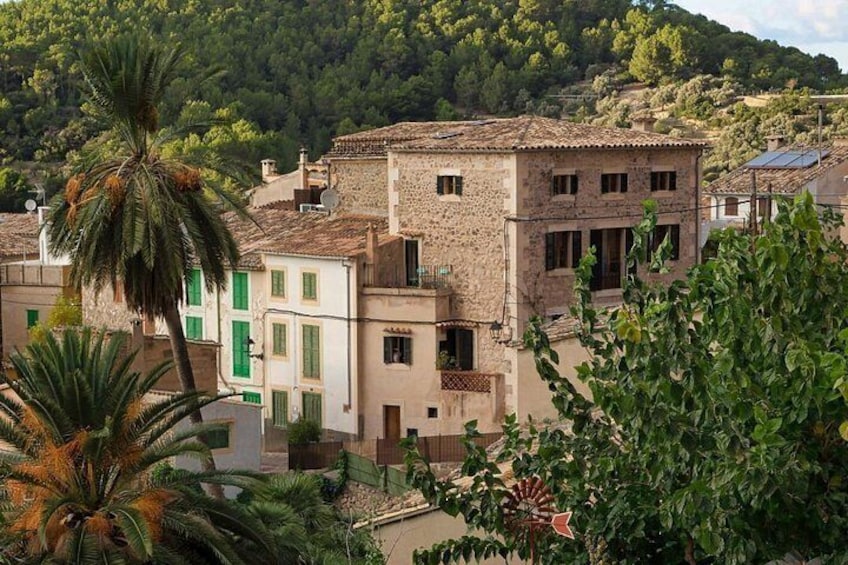 A stone building with a tiled roof, surrounded by greenery and trees. 2
