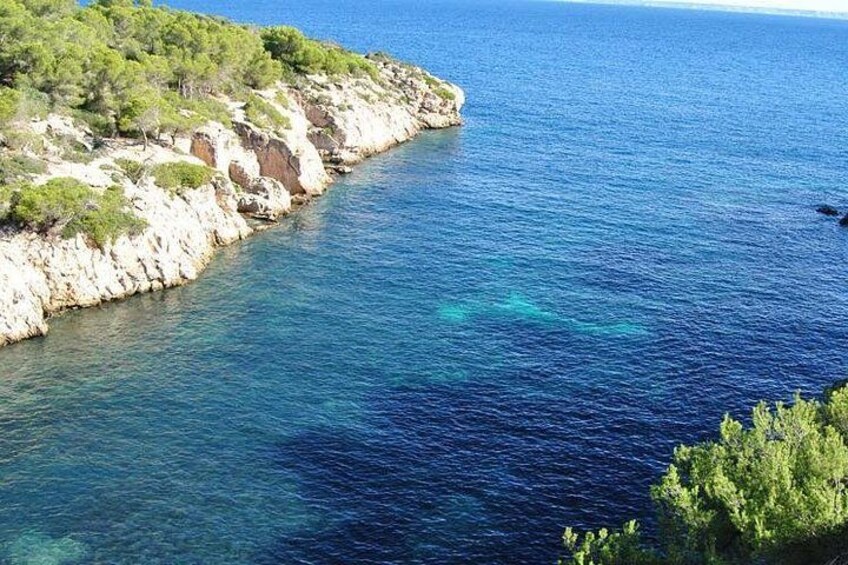 A coastal landscape with clear blue waters, rocky cliffs, and sparse vegetation. 3