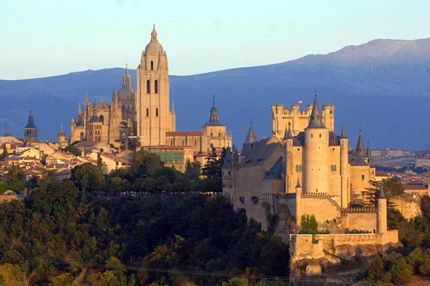 A historic castle with a prominent church, surrounded by a forested area and a mountain in the background. 5