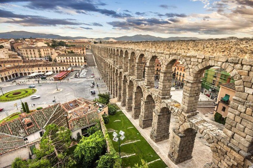 A historic stone aqueduct with arches, a plaza with a fountain, and surrounding buildings. 2