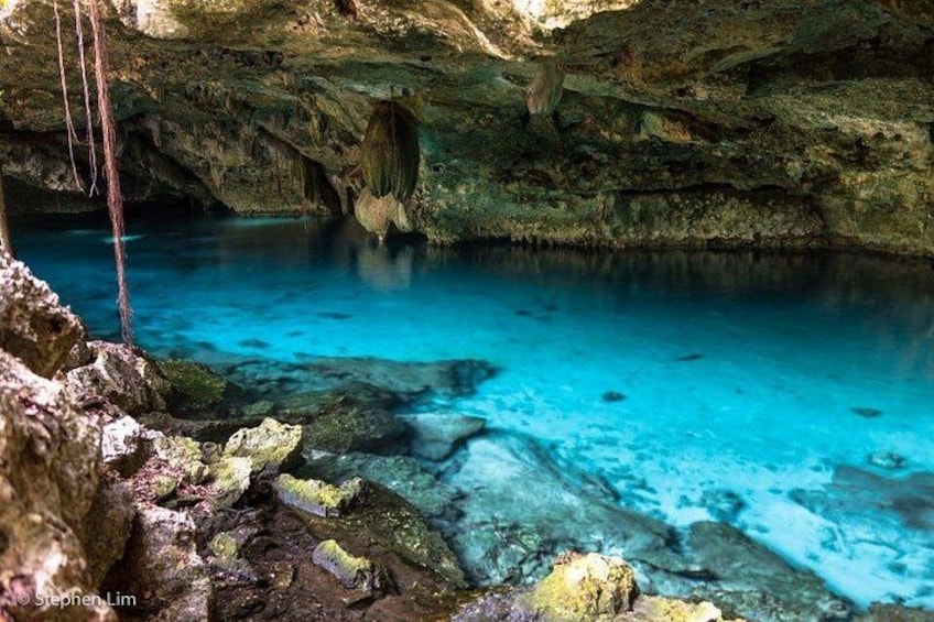 Una cueva con agua azul cristalina, formaciones rocosas y un estalactita colgante. 1