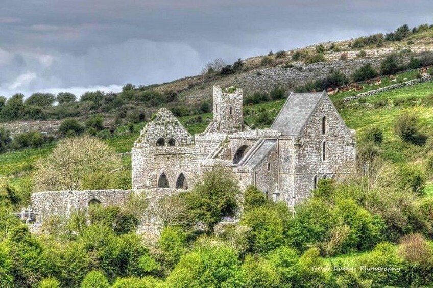 A stone church with arched windows and a bell tower, surrounded by greenery and hills. 2