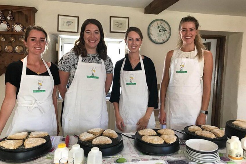 Four people wearing aprons with a logo, standing in front of a table with food items. 1