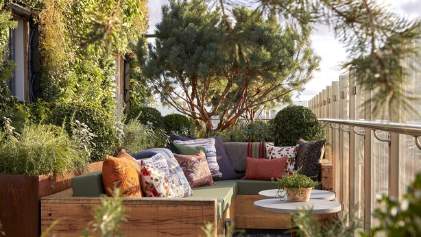 An outdoor seating area with a green sofa, multiple cushions, and a small table with a plant. - Treehouse Hotel London (London)