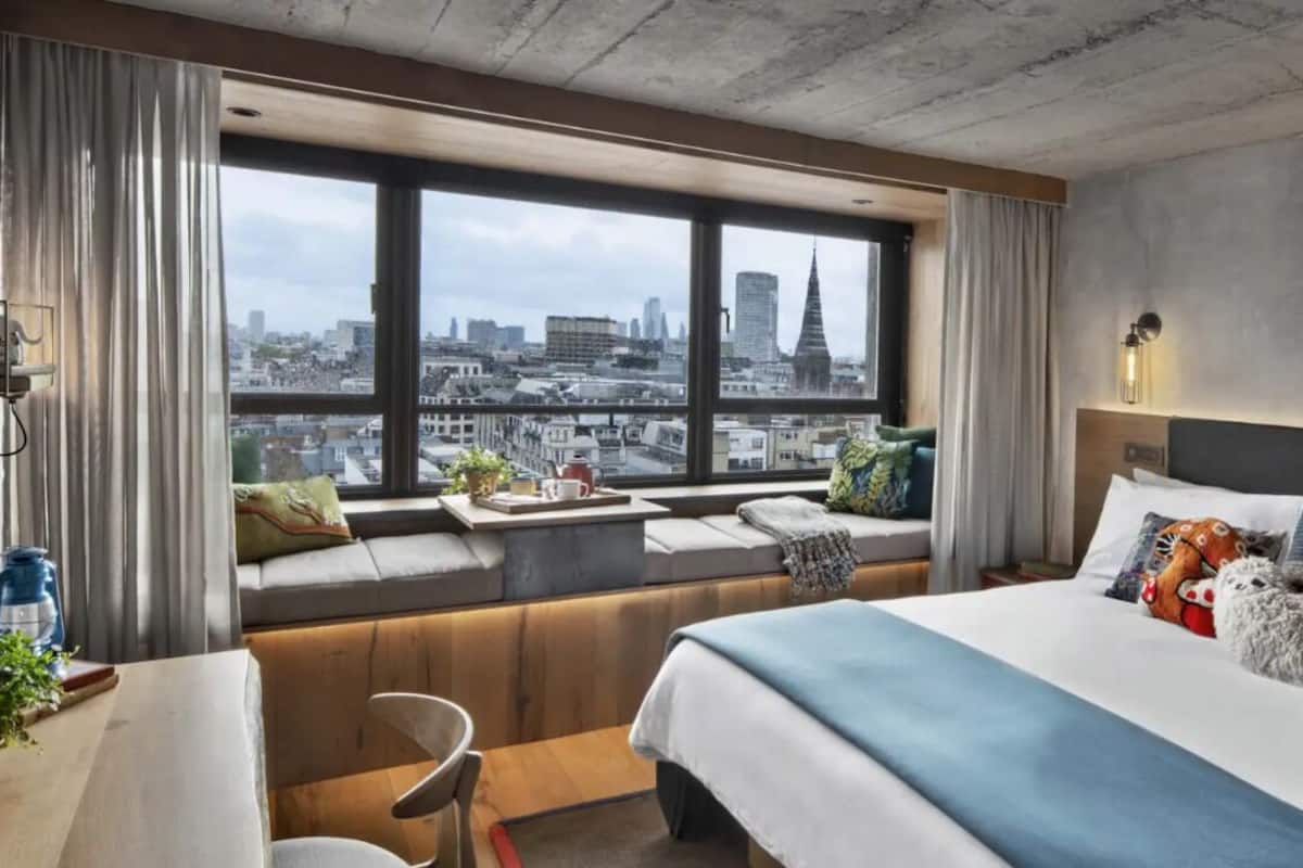 Habitación de hotel con un ventanal grande, una cama, zona de estar y una mesa con una planta.