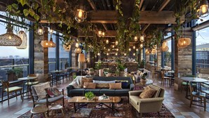A spacious lounge area with a large sofa, multiple chairs, and tables. The room features exposed wooden beams, hanging plants, and pendant lighting. - Treehouse Hotel London (London)