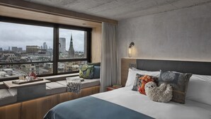 A modern hotel room with a large window offering a city view, a neatly made bed with decorative pillows, and a small table with a tray. - Treehouse Hotel London (London)