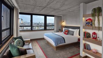 A modern bedroom with a large bed, a view of the city, a seating area, and a shelf with decorative items.