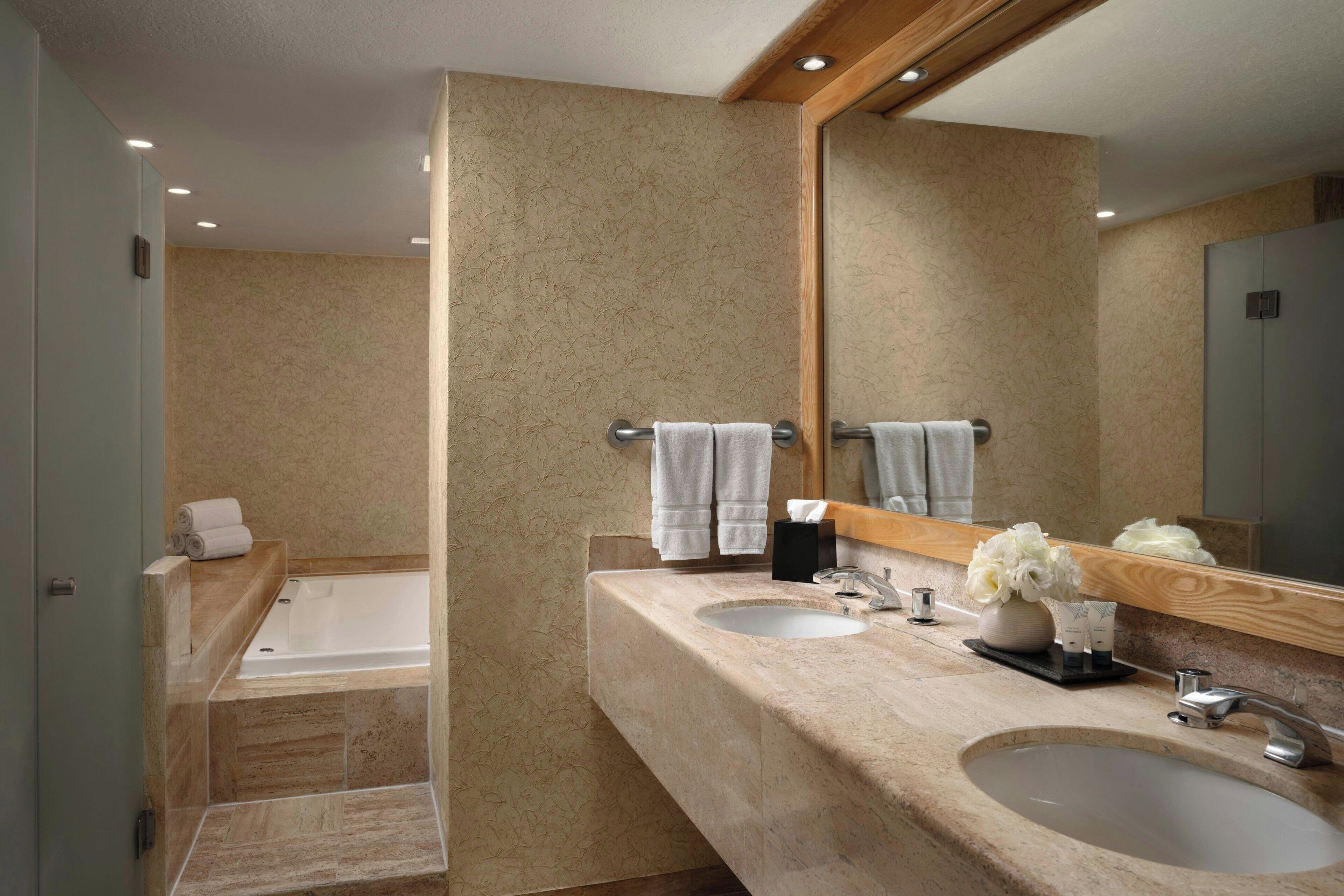 A bathroom with a bathtub, two sinks, a mirror, and towels.