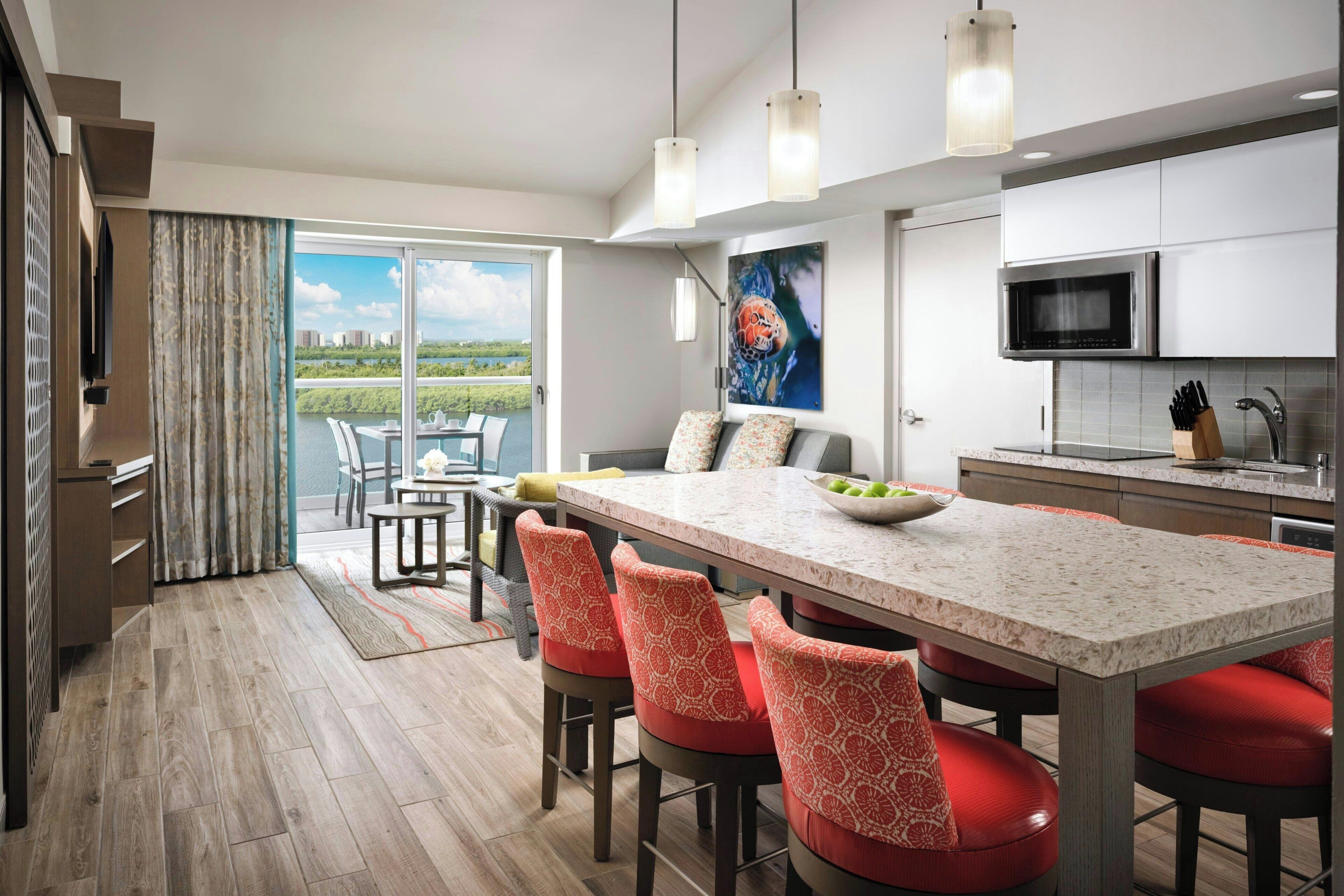 A modern kitchen with a large island, bar stools, a dining area with a view, and a flat-screen TV.