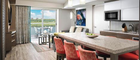 A modern kitchen with a large island, bar stools, a dining area with a view, and a flat-screen TV.