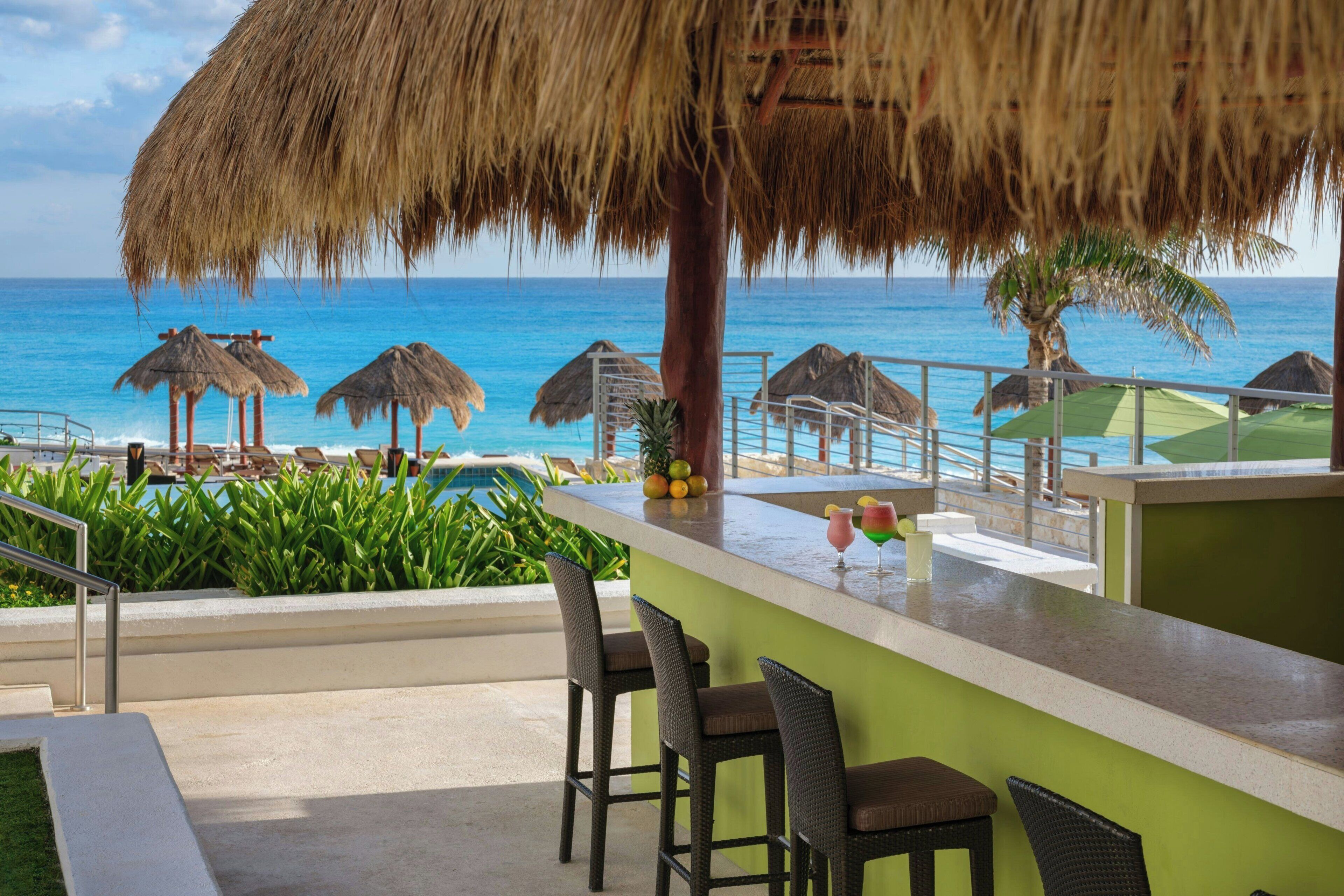 A beachside bar with a view of the ocean, thatched umbrellas, and lounge chairs.