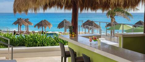 A beachside bar with a view of the ocean, thatched umbrellas, and lounge chairs.