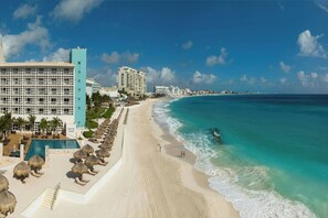 Un resort en la playa con piscina, tumbonas y vistas al océano.