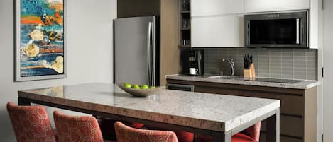 Una cocina moderna con encimera de mármol, electrodomésticos de acero inoxidable y taburetes de bar con estampado rojo.