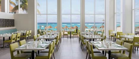 A restaurant with a view of the ocean, large windows, and yellow chairs.