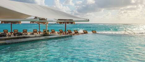 Ein Pool mit Liegestühlen und Sonnenschirmen mit Blick auf einen Strand.