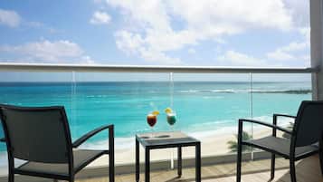 Un balcon avec deux chaises et une petite table, donnant sur une plage aux eaux bleu clair et sur une île lointaine.