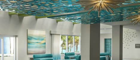 A modern lobby with teal sofas, a large abstract painting, and a ceiling with geometric cutouts.