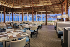 A restaurant with tables and chairs, large windows, and a view of the ocean. - The Westin Cancun Resort & Spa (Cancun)