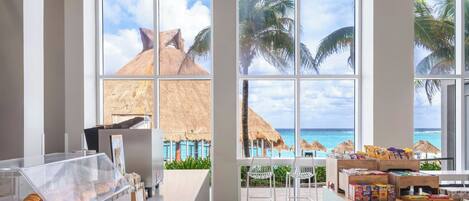 A room with large windows, a buffet counter with pastries, and a view of the ocean.