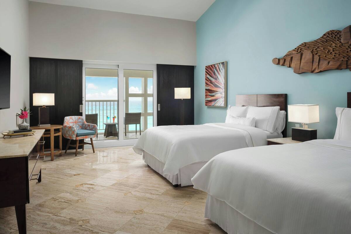 A hotel room with two beds, a desk, a chair, and a balcony with a view.