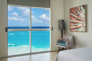 Habitación con un amplio ventanal corredera que da a vista de playa, una silla y un cuadro en la pared.
