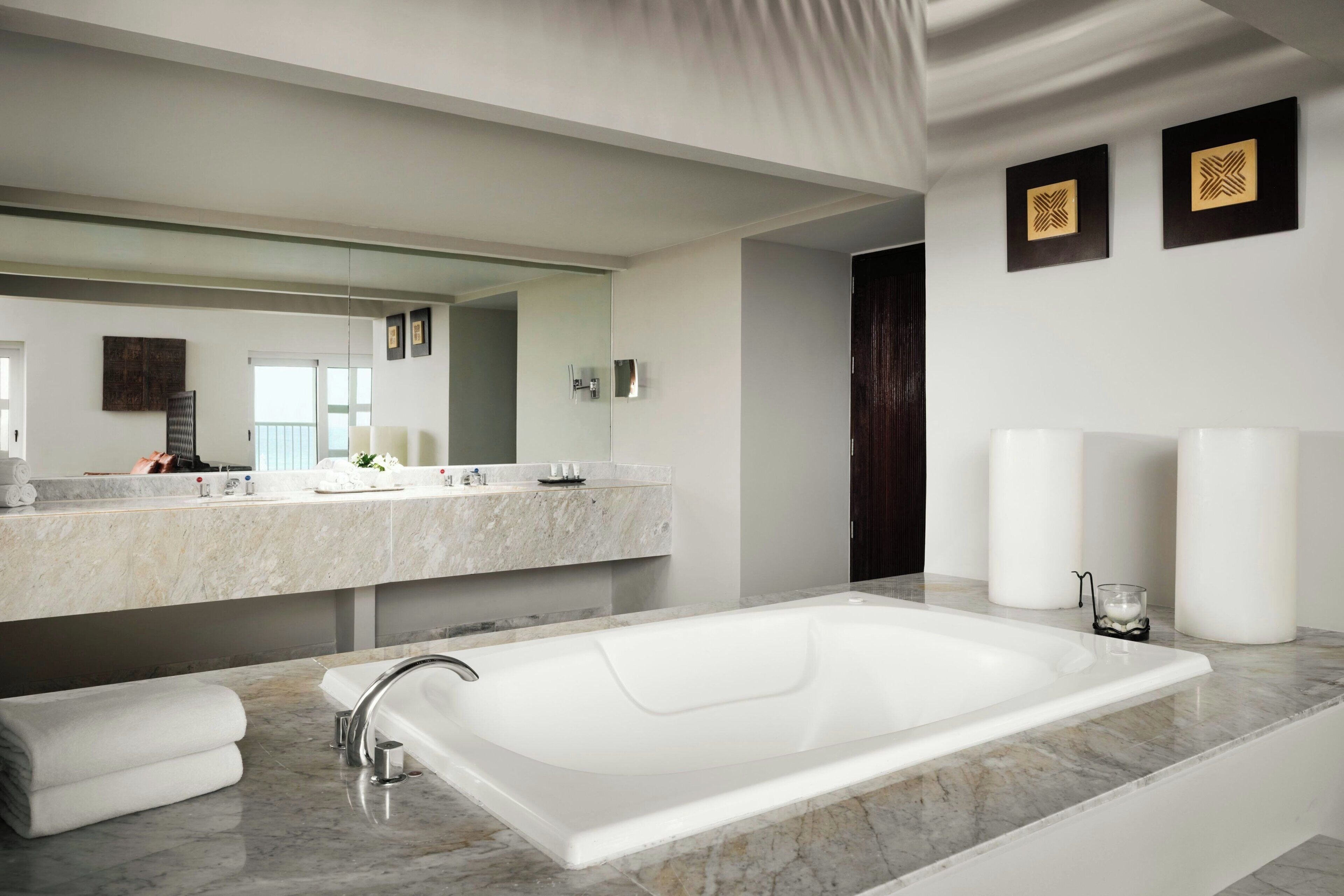 A modern bathroom with a large bathtub, a double vanity with a mirror, and a dark wooden door.