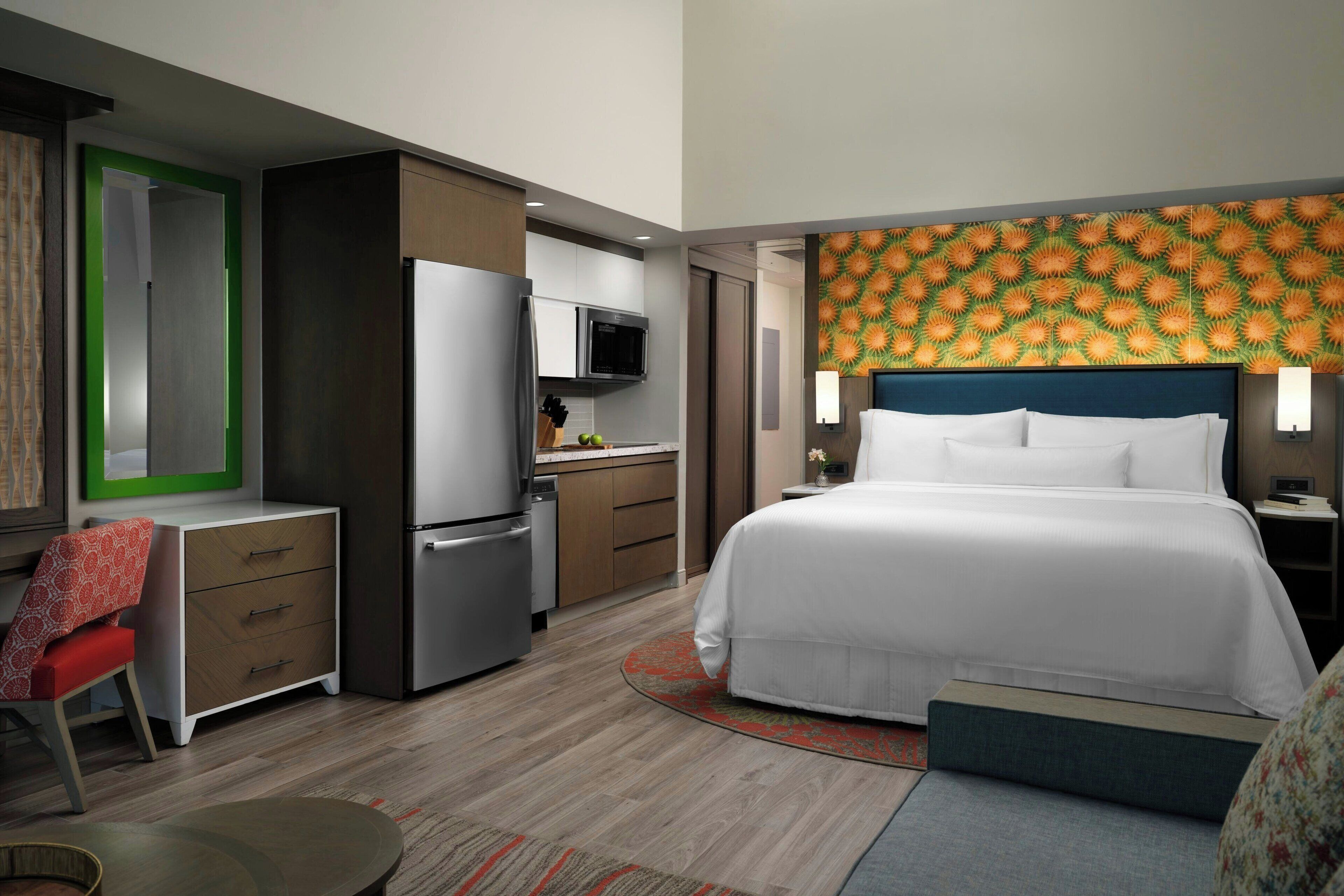 A hotel room with a bed, a desk, a kitchenette, and a bathroom.