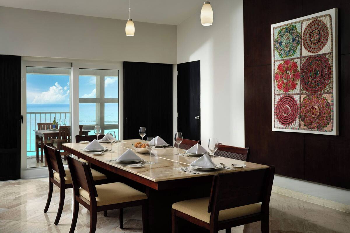 A dining area with a large table set for six, a view of the ocean, and a decorative wall panel.