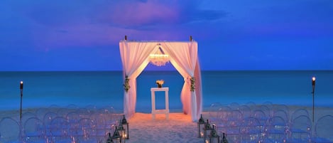 A beach wedding setup with a canopy, chairs, and lanterns.