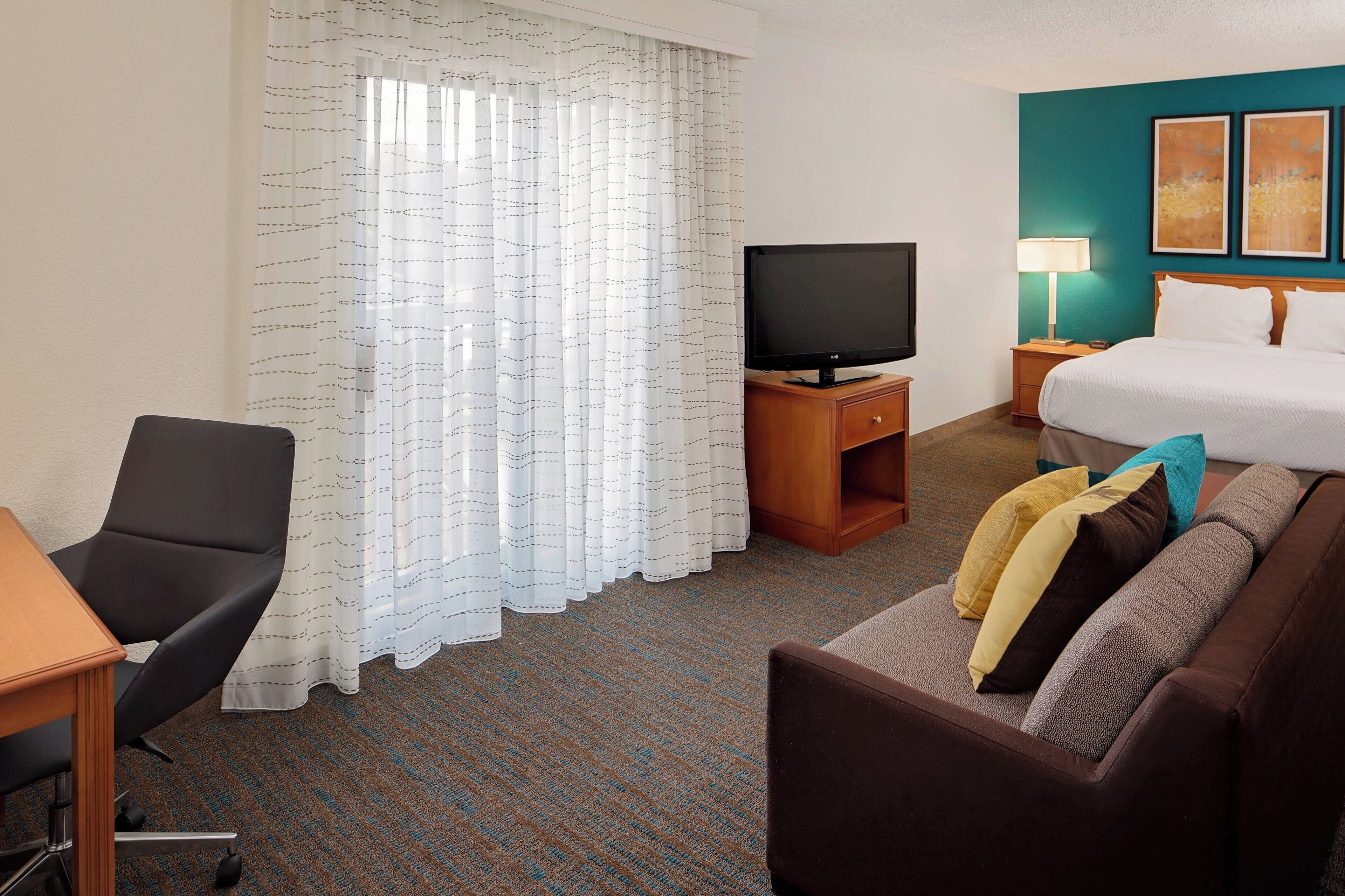 A hotel room with a bed, a TV, a desk, and a chair.