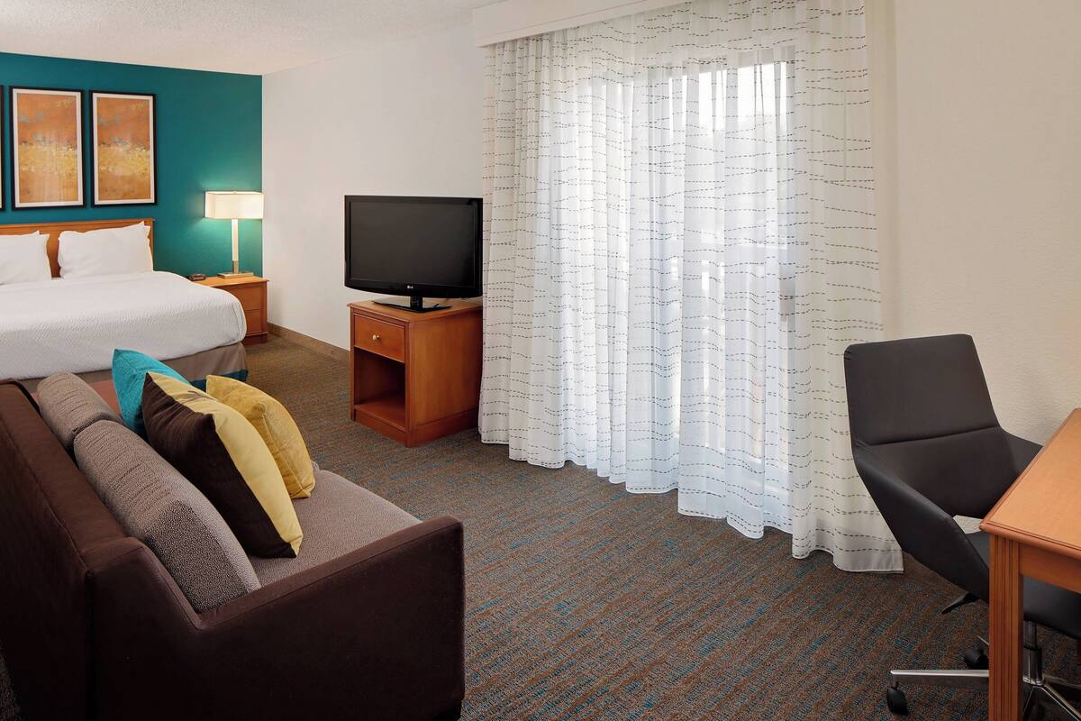 A hotel room with a bed, a TV, a desk, and a chair.