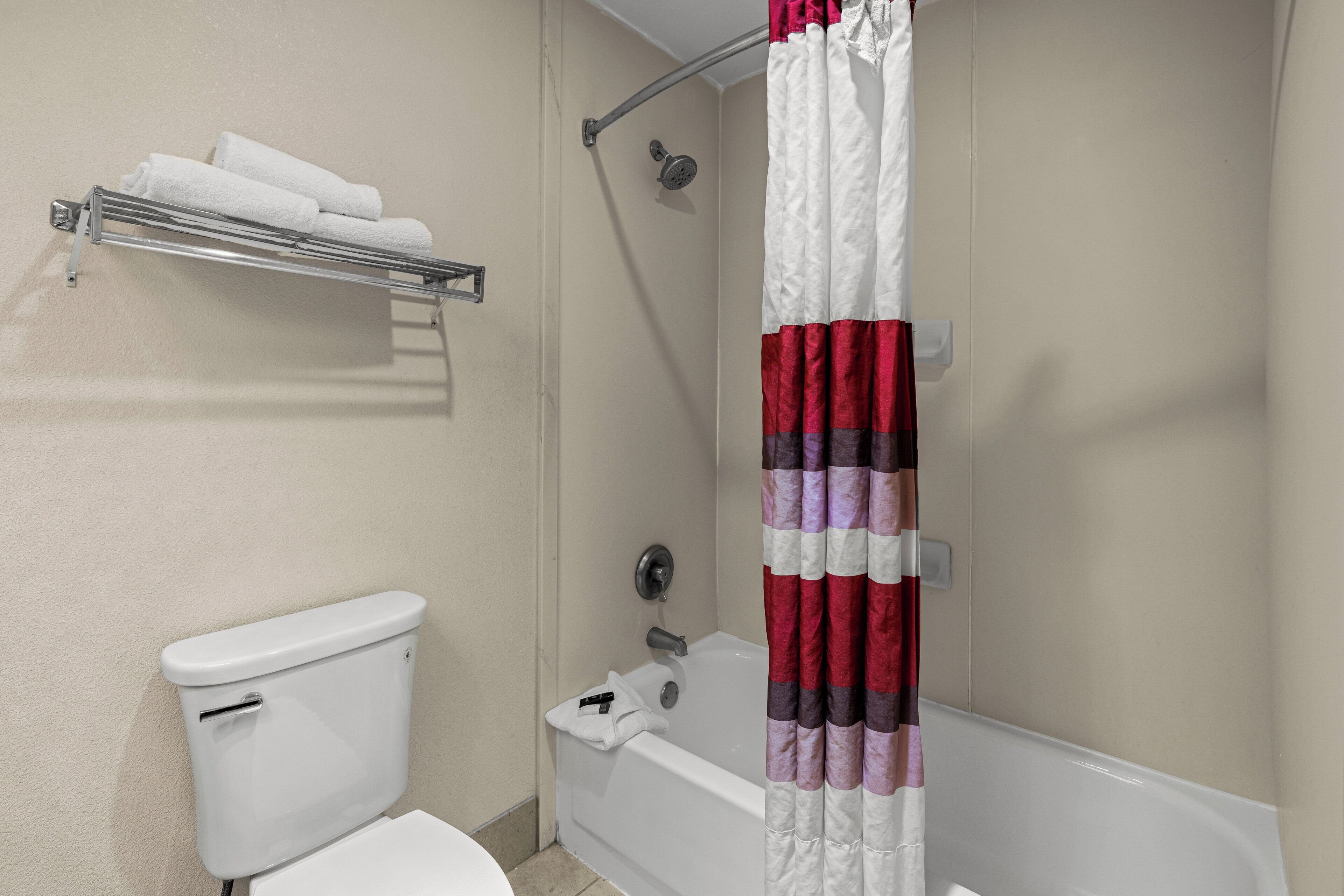 A bathroom with a toilet, a shower with a metal grab bar, and a towel rack with folded towels.