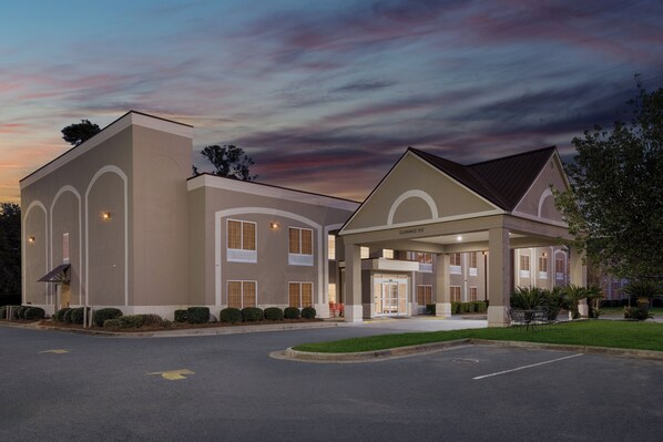 A hotel with a covered entrance, multiple windows, and a parking lot.