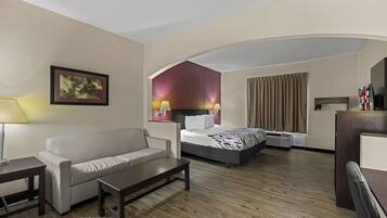 A hotel room with a sofa, a bed, a desk, and a lamp.