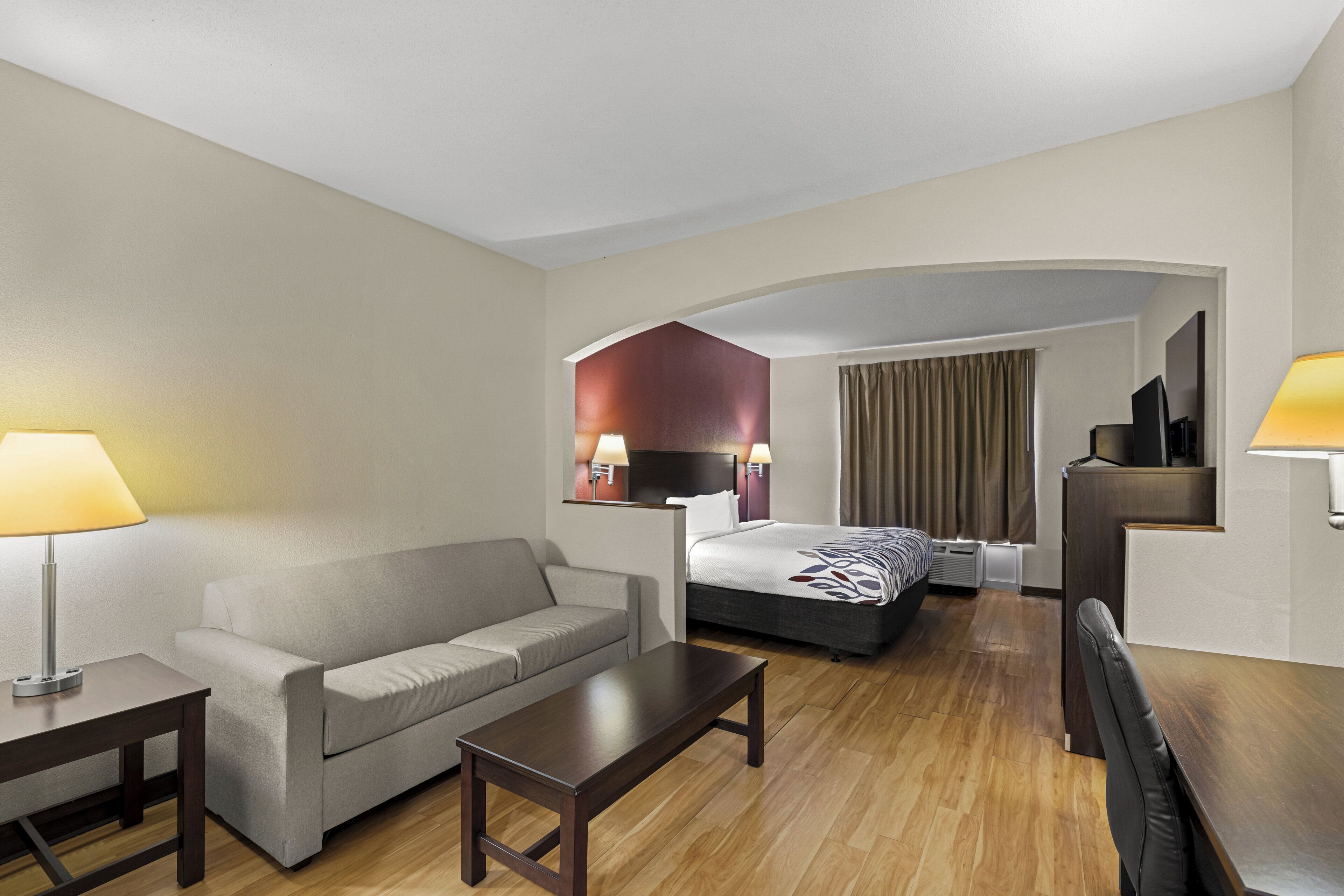 Una habitación de hotel con sofá, cama, escritorio, televisión y lámpara.