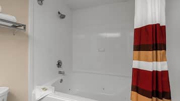 Une salle de bain avec une baignoire blanche, une pomme de douche, une serviette et un rideau de douche à rayures.