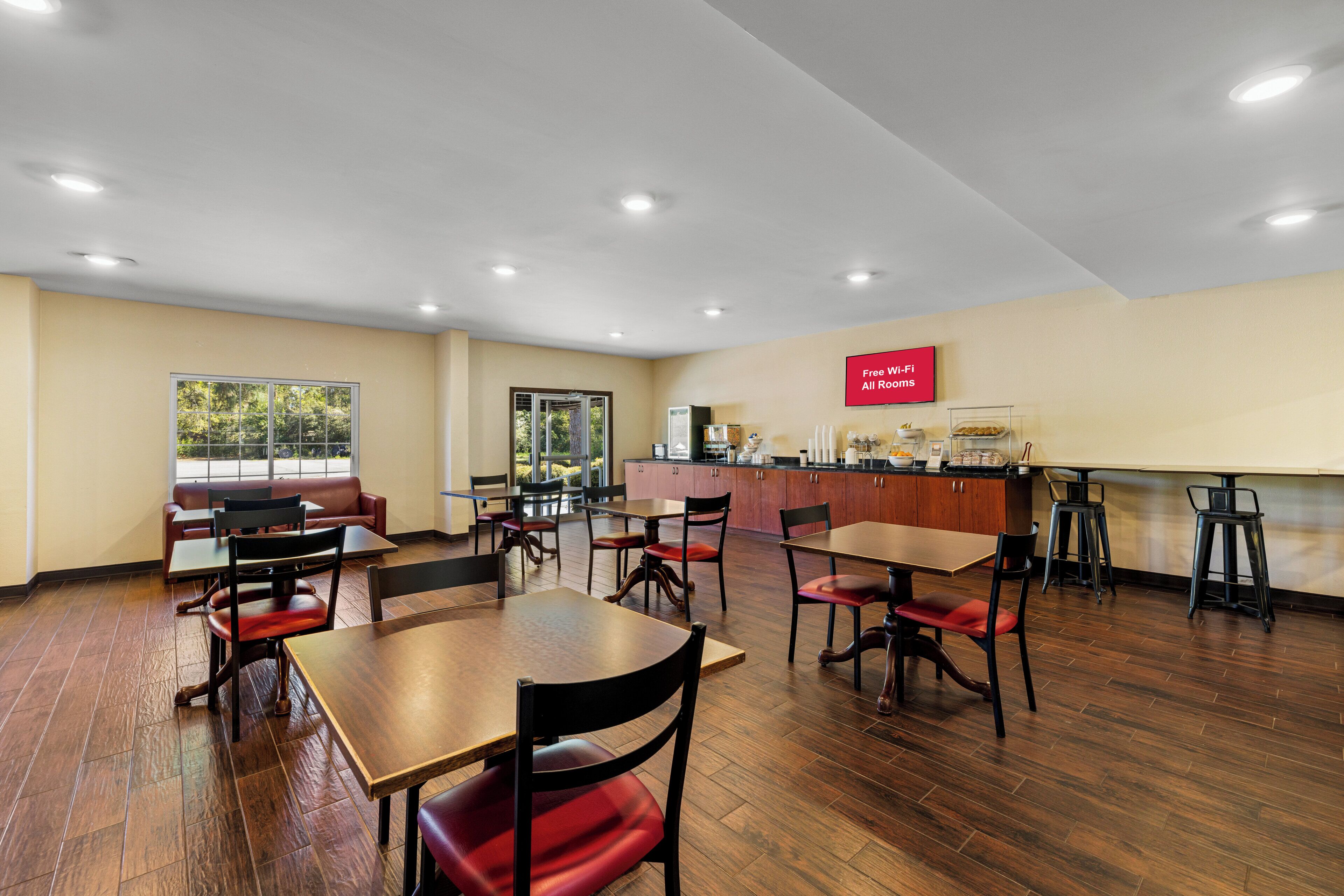 A spacious indoor area with multiple tables and chairs, a kitchen counter, and a large window providing natural light.