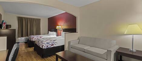 Quarto de hotel com cama, sofá, escrivaninha e televisão.