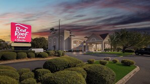 A hotel with a large sign for Red Roof Suites, surrounded by well-maintained hedges and a parking area. - Red Roof Inn & Suites Albany, GA (Albany)