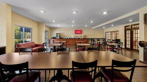 Un grand espace dédié à la salle à manger, avec plusieurs tables et chaises, un coin cuisine à l’arrière-plan et un panneau indiquant que le Wi-Fi est disponible gratuitement.