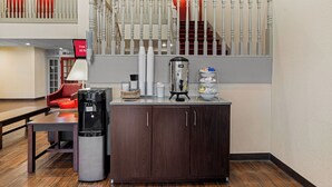 A hotel lobby with a coffee machine, a trash can, and a seating area with a red chair. - Red Roof Inn & Suites Albany, GA (Albany)