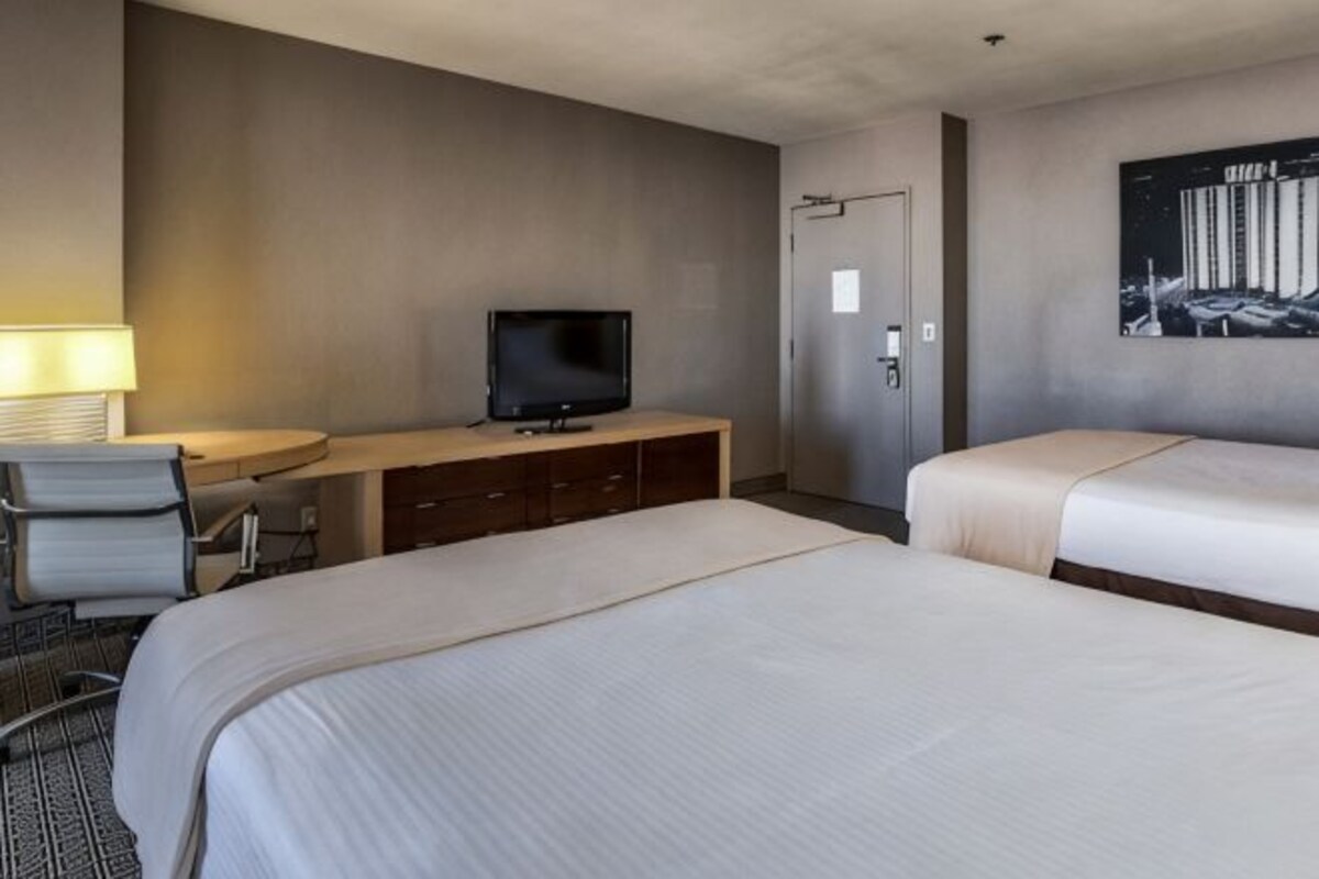A hotel room with a bed, a desk with a television, a chair, and a door.