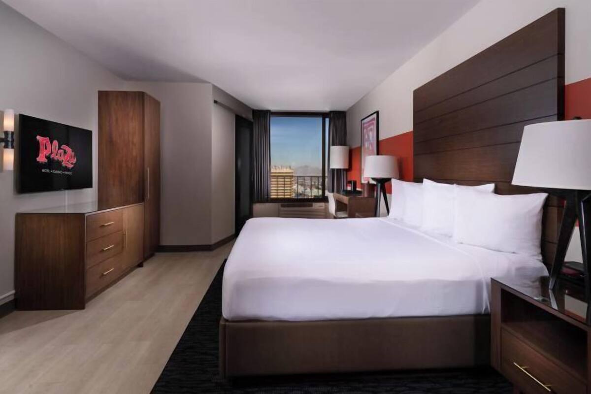 A hotel room with a large bed, a TV, a desk, and a view of a cityscape.