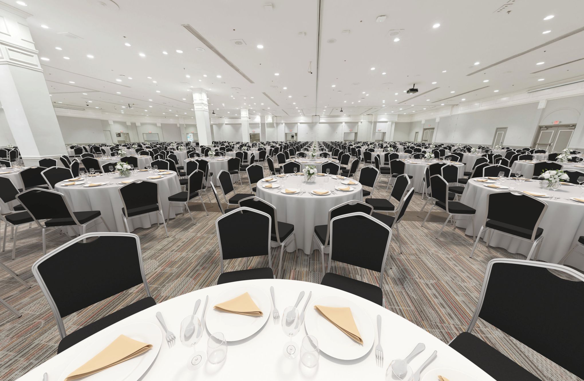 Une vaste salle de banquet dotée de nombreuses tables rondes, chacune recouverte d’une nappe blanche et agrémentée de chaises noires et de couverts disposés avec soin.