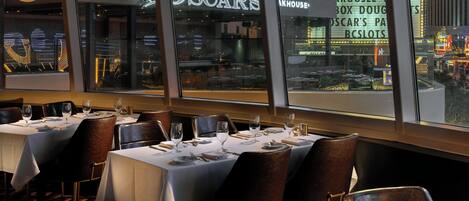 Un restaurante con mesas dispuestas para comer, vista a la calle y un letrero de neón que dice 'Oscar's'.
