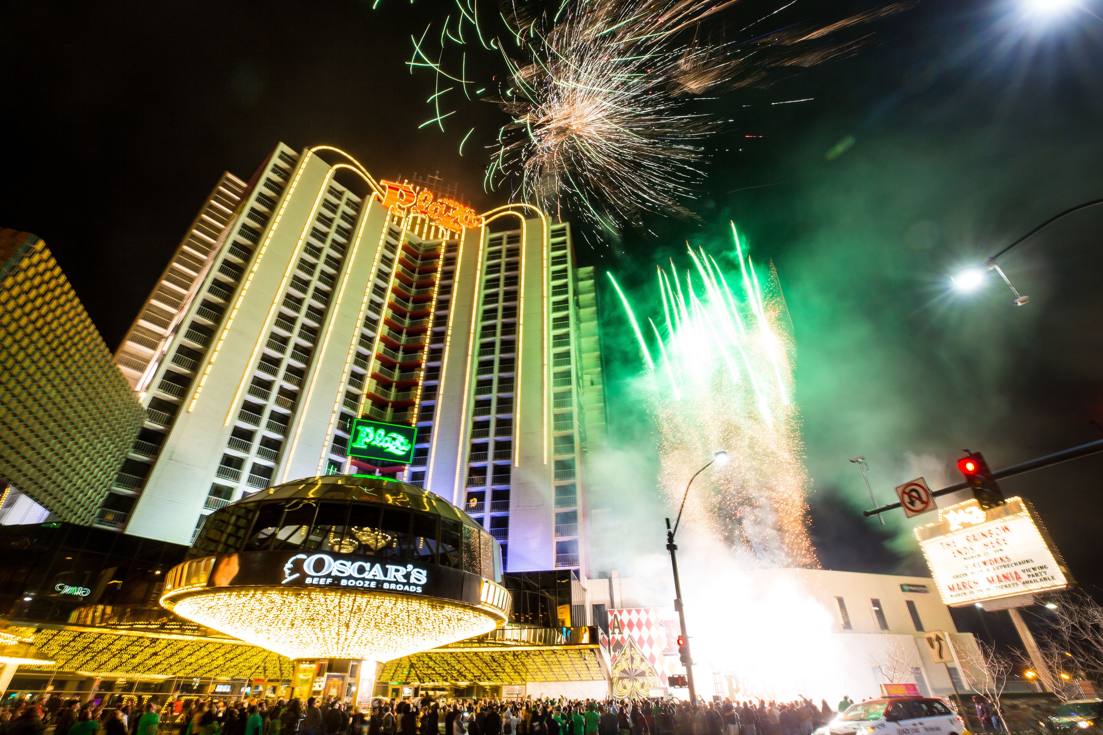 A building with a large illuminated sign, a crowd of people, and fireworks in the background.