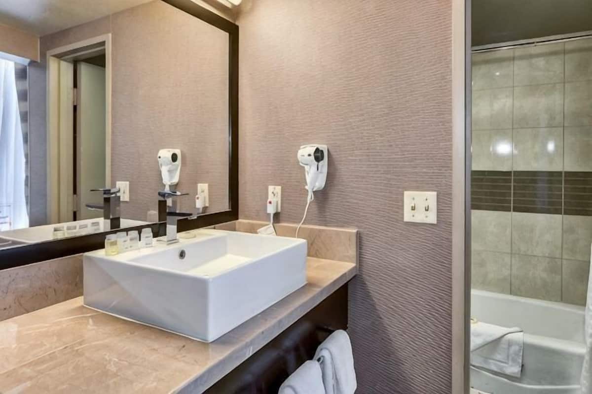 A bathroom with a large mirror, two hair dryers, a sink, and a shower.
