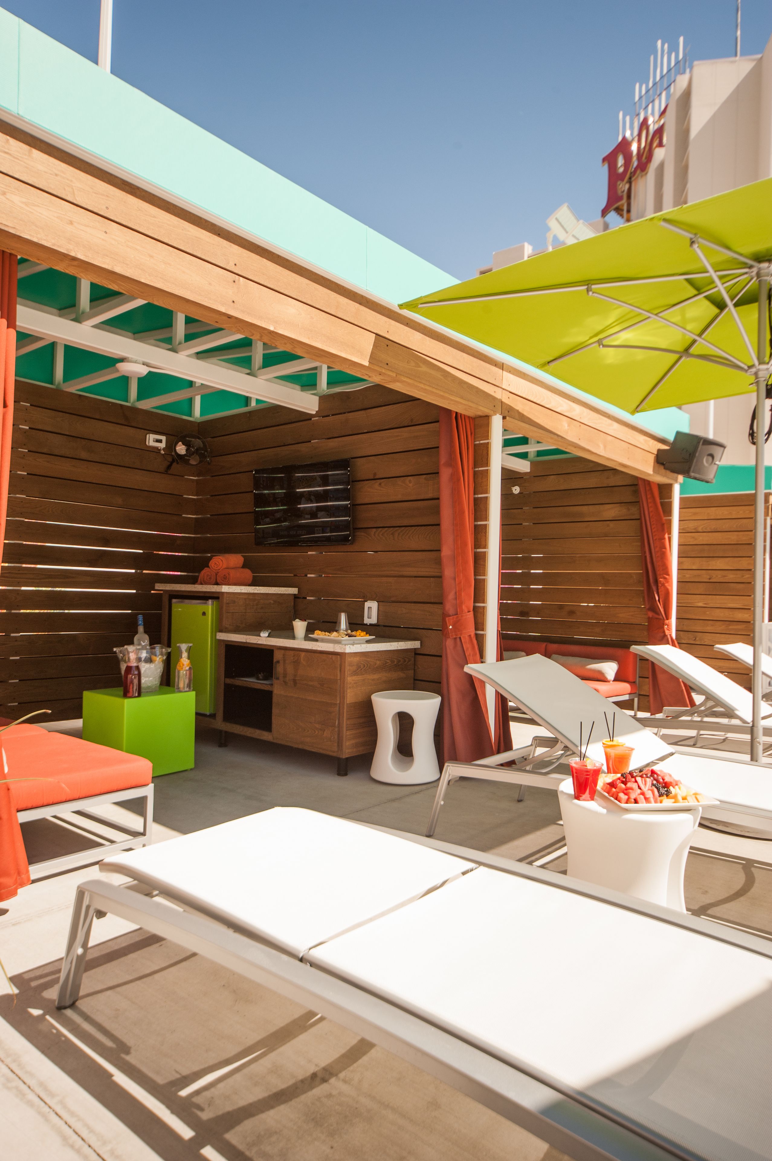 Un espace extérieur ensoleillé, aménagé avec des murs en bois, une table verte, des fauteuils blancs et un parasol jaune.